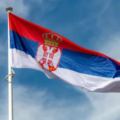 The national flag of Serbia waving in a blue, slightly clouded sky. 
