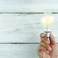 hand holding light bulb on a white wooden background