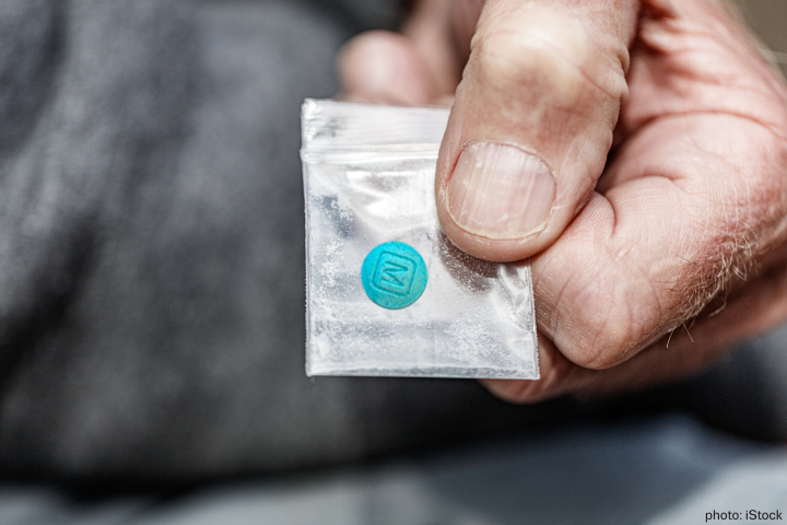 A male hand holding a small plastic bag with a blue pill