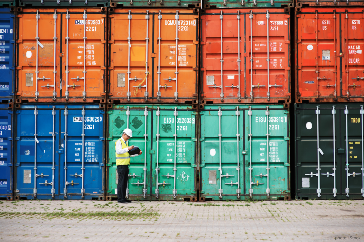 Man in a yellow vest standing in front of shipping containers